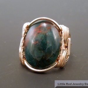 May include: A green, red, and brown oval gemstone ring with a gold wire wrapped setting.