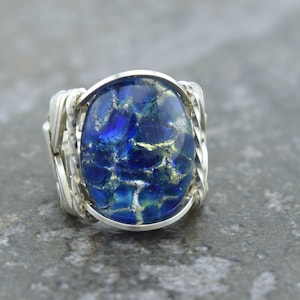 May include: A silver ring with a blue and gold dichroic glass oval cabochon set in a twisted wire band.