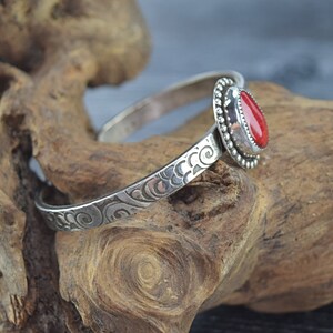 May include: A silver bangle bracelet with an ornate design and a red gemstone set in a silver bezel.