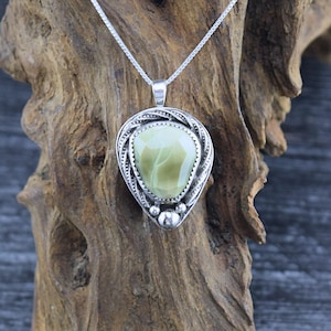 May include: A silver pendant necklace with a green and white stone set in a silver frame. The pendant is shaped like a teardrop and has a beaded detail at the bottom.