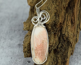 May include: A silver wire wrapped pendant featuring a pink and white oval shaped gemstone. The pendant is hanging from a silver chain.