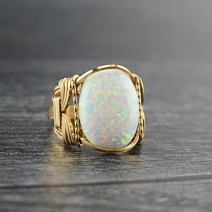 May include: A gold wire wrapped ring with a white opal gemstone. The opal has a rainbow iridescent sheen.