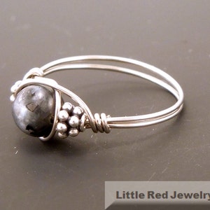 May include: A silver ring with a black gemstone wrapped in wire. The ring is set with small silver beads.