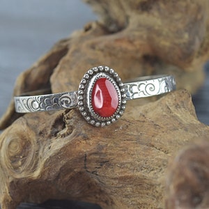 May include: A silver bangle bracelet with an ornate design and a red gemstone set in a silver bezel.