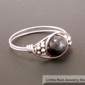 May include: A silver ring with a black gemstone and silver beads. The ring is made of wire and has a simple design.