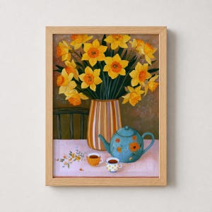 Può includere: Un dipinto incorniciato raffigurante un bouquet di narcisi giallo brillante in un vaso a righe, posto accanto a una teiera color ottanio con motivi floreali arancioni e due piccole tazze abbinate su una superficie chiara.