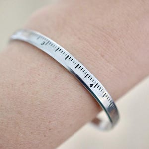 May include: A silver bracelet with a ruler design. The bracelet has markings from 3 to 4 inches.