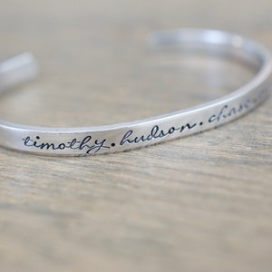 May include: A silver bangle bracelet with the inscription "timothy. hudson. charm"