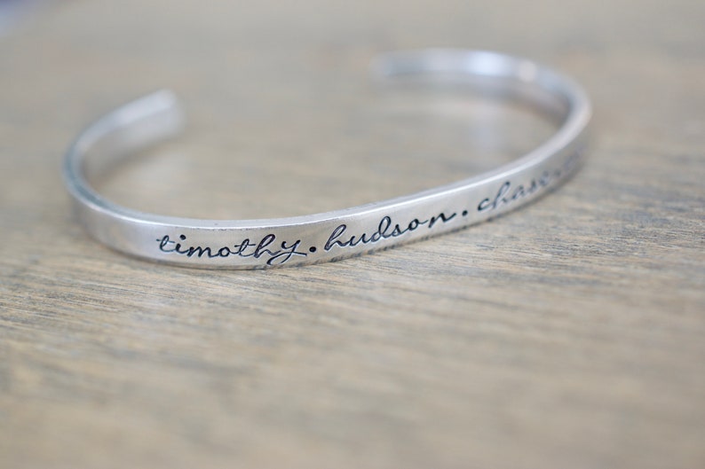 May include: A silver bangle bracelet with the inscription "timothy. hudson. charm"
