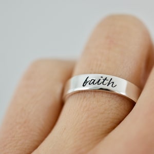 May include: A silver band ring with the word "faith" engraved on it.