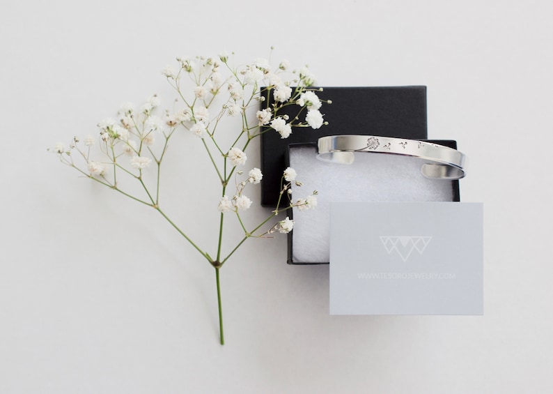 May include: A silver bangle bracelet with a delicate floral design, packaged in a black box with white tissue paper and a small card with the text "www.daintyjewelry.com".
