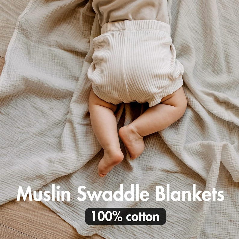 K&ouml;nnte beinhalten: Ein Baby liegt auf einer hellgrauen Musselin-Swaddle-Decke und tr&auml;gt cremefarbene gerippte Shorts. Die Decke besteht aus einem weichen, strukturierten Stoff. Der Text auf dem Bild lautet "Muslin Swaddle Blankets" und "100% cotton."