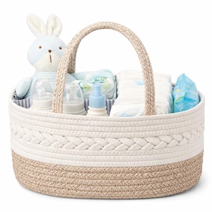 May include: A cream and tan woven rope basket with a braided handle, containing baby items. It features a blue bunny toy, baby bottles, nappies, wipes, and a blue lotion dispenser. A practical and stylish baby care organiser.