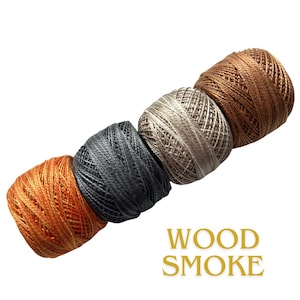 May include: Four spools of thread in a diagonal row. Colors include orange, dark gray, light gray, and brown. The text "WOOD SMOKE" is in gold letters below the spools.