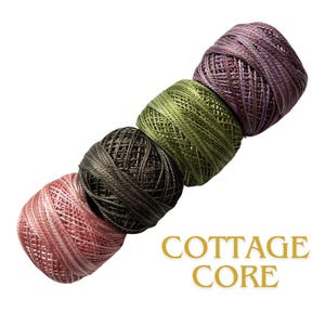 May include: Four spools of colorful thread in shades of pink, brown, green, and purple are arranged diagonally. The text "COTTAGE CORE" is displayed in gold below the spools. The thread appears to be for crafting or embroidery.