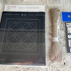 May include: A black fabric with a white geometric pattern for sashiko embroidery. The kit includes beige embroidery floss, two needles, and instructions in Japanese.