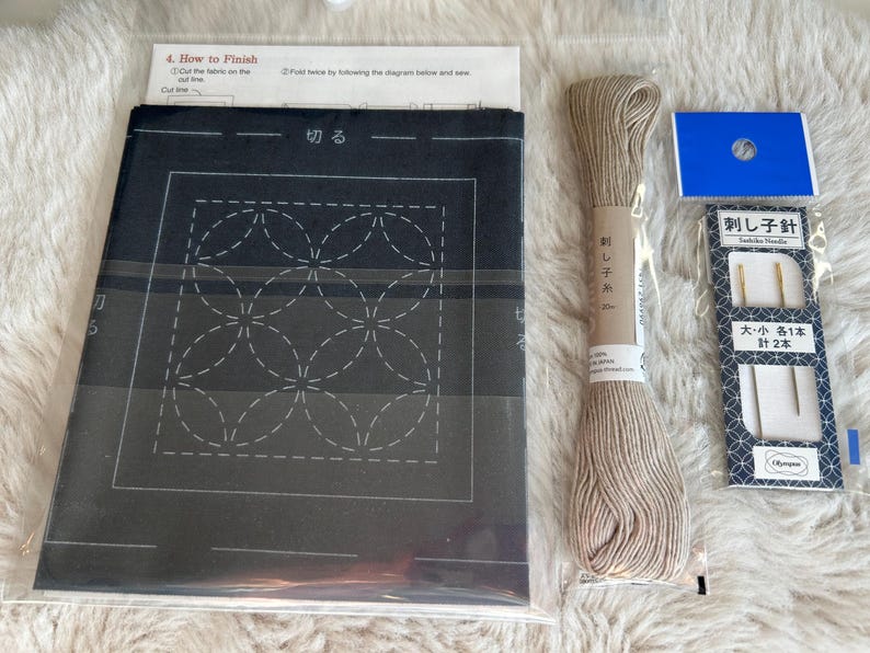 May include: A black fabric with a white geometric pattern for sashiko embroidery. The kit includes beige embroidery floss, two needles, and instructions in Japanese.