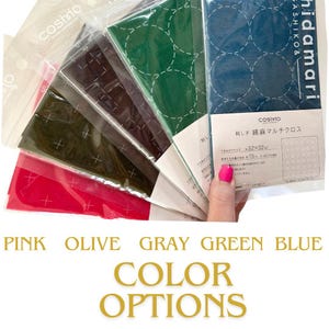 May include: A selection of Cosmo brand sashiko fabric in various colors, including pink, olive, gray, green, and blue. Each fabric piece is packaged in a clear plastic sleeve. The text "COLOR OPTIONS" is displayed below the fabric.