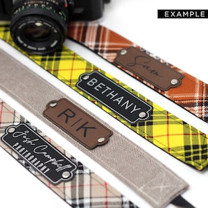 May include: Four camera straps with different plaid patterns and personalized leather name tags. The name tags read "Bethany", "Rik", "Josh Campbell Photography", and "Sarah".