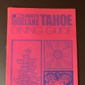 May include: A pink pamphlet with a blue title "North Lake Tahoe Dining Guide". The cover features a geometric design with a variety of shapes and patterns in blue.