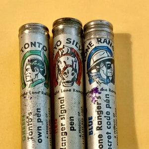 May include: Three silver metal pens with colorful labels featuring illustrations of characters from the Lone Ranger and Tonto. The labels read "Tonto's own pen", "danger signal pen", and "Lone Ranger's secret code pen".