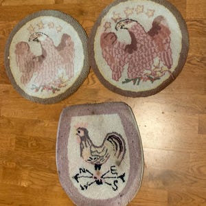 May include: Three vintage, hand-stitched rugs. Two round rugs feature a pink eagle design with stars. The third rug is oval-shaped and displays a rooster with a compass design. All rugs have a light beige background and a brown border.