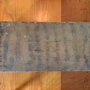 May include: A weathered wooden box with a worn, faded surface. The box is made of wood planks and has a rectangular shape. The box is empty and has no visible markings or labels.