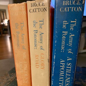 May include: Three hardcover books with blue, white, and orange covers. The books are part of a series titled "The Army of the Potomac" by Bruce Catton. The titles are "A Stillness at Appomattox", "Glory Road", and "Mr. Lincoln's Army".