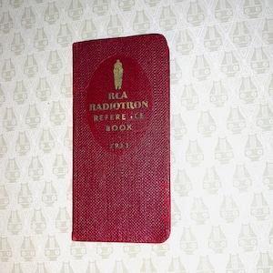 May include: A vintage red RCA Radiotron Reference Book from 1933. The book has gold lettering and a circular emblem. The cover has a textured appearance.