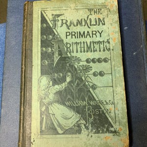 May include: An antique book titled "The Franklin Primary Arithmetic" with a green and black cover. The cover features an illustration of a girl and an abacus. The book is worn, with visible signs of age and use.