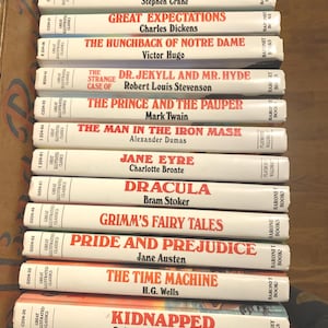 May include: A stack of twelve Great Illustrated Classics books with white spines and red text. Titles include The Merry Adventures of Robin Hood, The Red Badge of Courage, Great Expectations, The Hunchback of Notre Dame, Dr. Jekyll and Mr. Hyde, The Prince and the Pauper, The Man in the Iron Mask, Jane Eyre, Dracula, Grimm's Fairy Tales, Pride and Prejudice, The Time Machine, and Kidnapped.