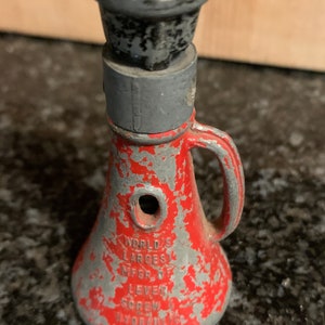 May include: A red and silver metal screw jack with the text "WORLD'S LARGEST MFG'R. OF LEVER SCREW & HYDRAULIC JACKS" on the side.
