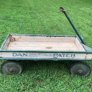 May include: A vintage wooden wagon with a green painted frame and a long metal handle. The side panels are white with the text DAN PATCH printed in black lettering. It features four dark green metal wheels and a natural wood interior base.