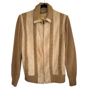 May include: A tan and brown zip-up jacket with a ribbed collar and cuffs. The jacket features a suede-like center panel with vertical cable knit detailing and knit sleeves. The jacket is hanging on a black hanger.