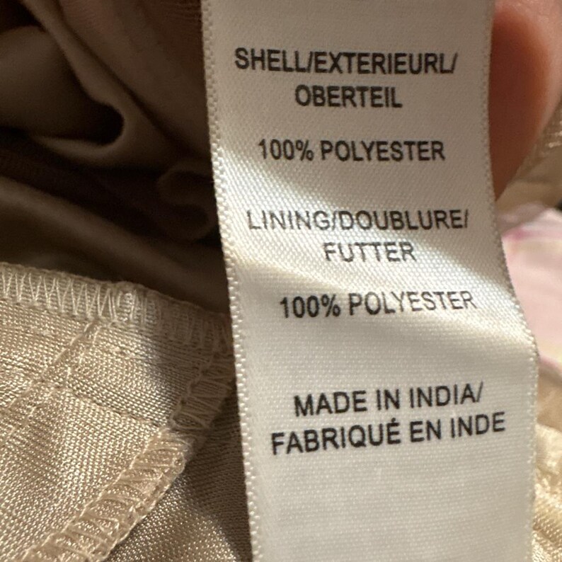 May include: Close-up of a fabric tag with text. The tag reads "SHELL/EXTERIEURL/OBERTEIL 100% POLYESTER" and "LINING/DOUBLURE/FUTTER 100% POLYESTER". The tag also states "MADE IN INDIA/FABRIQU&Eacute; EN INDE".