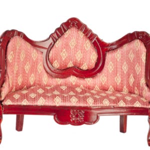 Puede incluir: Un sofá en miniatura y ornamentado, con estructura y patas de madera de color rojo oscuro. El asiento y el respaldo están tapizados en tela roja con un patrón de diamantes repetido en un color más claro. El sofá tiene un respaldo en forma de corazón.