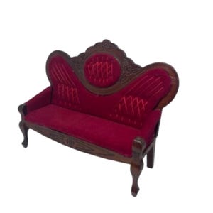 May include: Miniature Victorian-style sofa with a deep red velvet seat and back. The wooden frame is intricately carved and stained a dark brown. The sofa has curved arms and legs, and a decorative back.