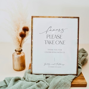 Op de afbeelding: Een wit bord met een gouden rand en een gegolfde rand met de tekst "favors please take one". Onder de tekst staat "Thank you for celebrating with us" en de namen "Sally and Anthony" met de datum "November 10th 20XX".