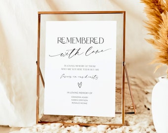 May include: A white sign in a gold frame with the text "Remembered with love" and "In loving memory of those who are not here today but are forever in our hearts." The sign also includes the names "Grandma Ashby, Karen Geryon, Ronald McRae".