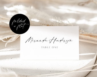May include: White card with black text that reads "Miranda Henderson, Table One". The card is sitting on a white surface with a white feather.