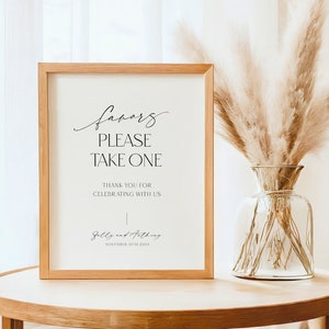 Op de afbeelding: Een ingelijst bord met de tekst "favors please take one" en "Thank you for celebrating with us", gevolgd door de namen "Sally and Anthony" en de datum "November 10th 20XX".