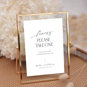 Op de afbeelding: Een wit bord in een gouden lijst met de tekst "favors please take one" en "Thank you for celebrating with us."  Het bord bevat ook de namen "Sally and Anthony" en de datum "November 10th 20XX".