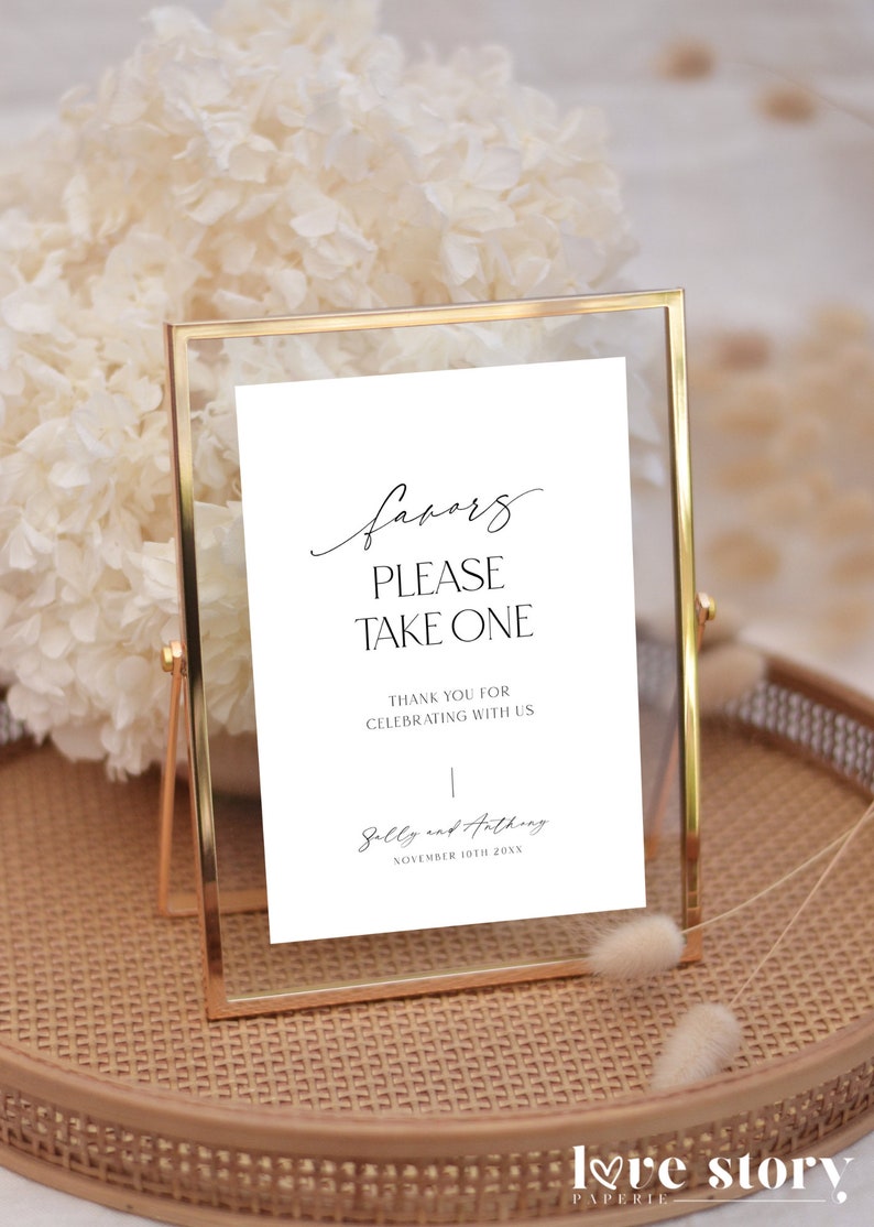 Op de afbeelding: Een wit bord in een gouden lijst met de tekst "favors please take one" en "Thank you for celebrating with us."  Het bord bevat ook de namen "Sally and Anthony" en de datum "November 10th 20XX".