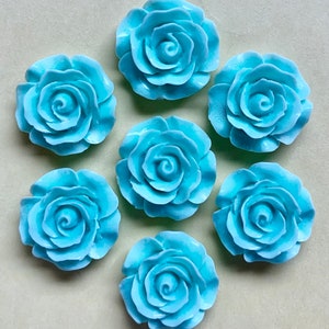 May include: Seven light blue ceramic rose embellishments. Each rose has a raised, detailed design and a slightly curled edge.