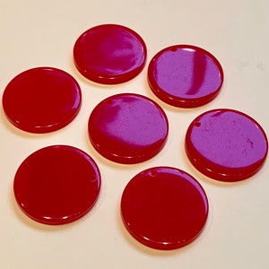 May include: Seven round, flat, red and purple plastic discs with a small hole in the center.