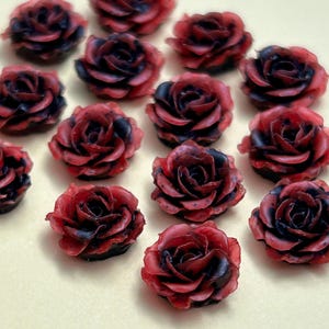 May include: A collection of 15 small, red and black rose-shaped resin embellishments. The roses have a layered, textured appearance.