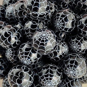 Peut inclure: Gros plan sur un tas de perles rondes noires et blanches avec un motif de toile d'araignée. Les perles sont en matériau brillant et ont un effet 3D.