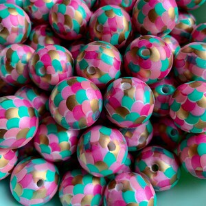 Puede incluir: Un montón de cuentas grandes, redondas y de madera con un patrón de escamas de sirena. Las cuentas están pintadas en tonos de rosa, verde azulado y dorado.