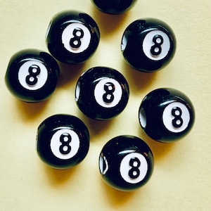 May include: Eight black and white 8-ball beads with white numbers on a light yellow surface.