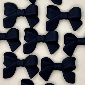 May include: A collection of nine black fabric bows. The bows are all the same size and shape, and they are arranged in a random pattern.